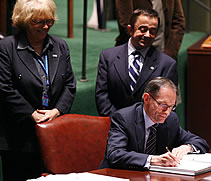 Ambassador signs document observed by Steve Estey and Dulcie McCallum